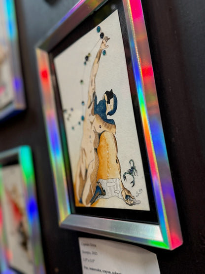 A framed art print featuring a stylized figure in beige, black, and blue tones, displayed on a dark wall with a holographic iridescent frame.