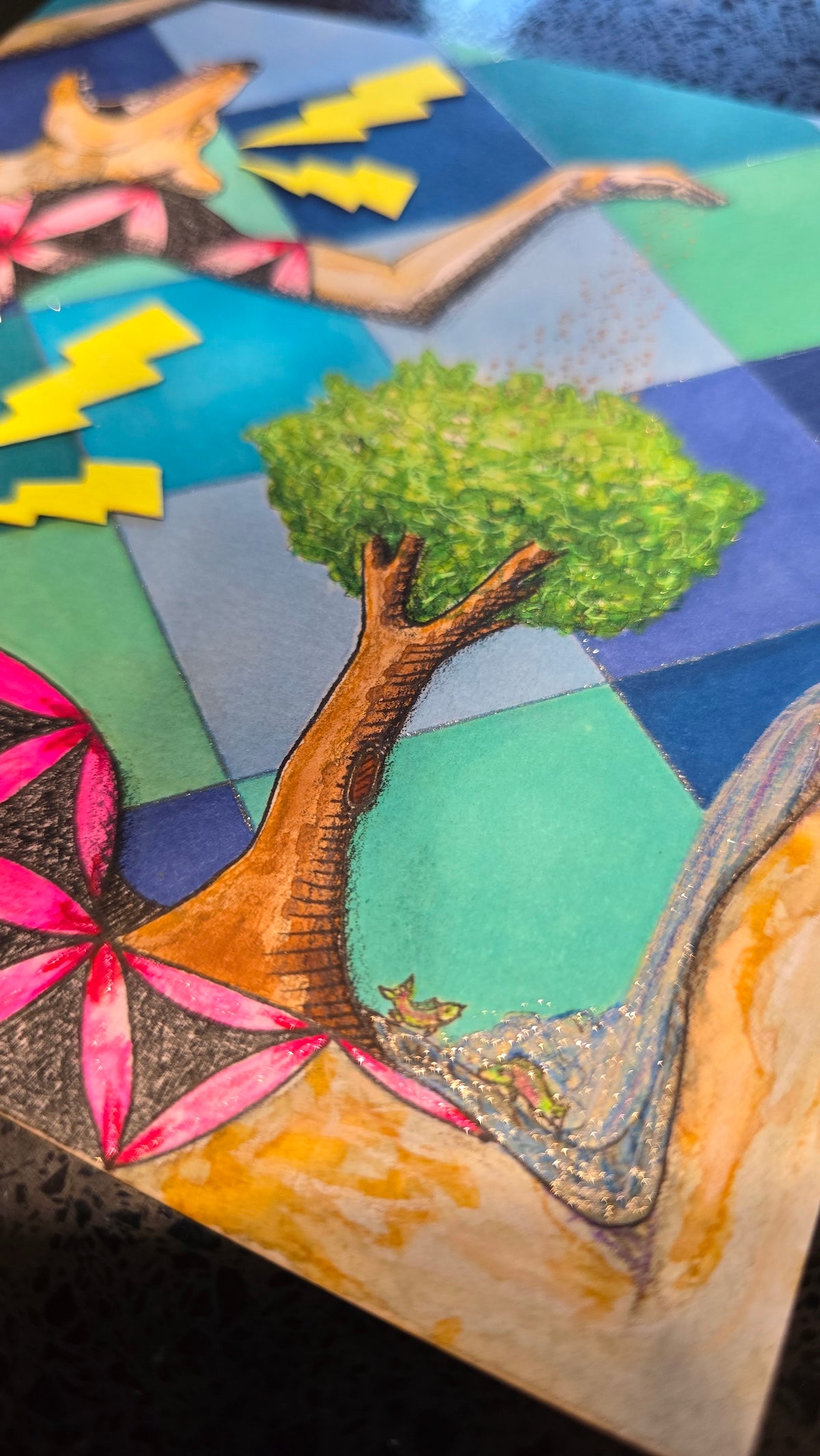 A close-up of a colorful mixed-media artwork depicting a stylized tree with a brown trunk and green textured foliage, set against a geometric background of blue, green, and yellow shapes.